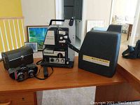 Overview of binoculars, projector, projector cover, and binoculars case set on wooden table with indoor background