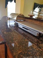 Brass chafing dish with wood trim and dome cover on a kitchen counter next to a warming tray