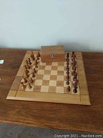 Photo showing entire chessboard set up with chess pieces and wooden storage box on top of board.
