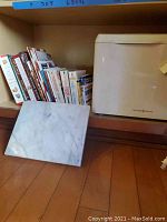 Shelf with cookbooks, marble cheese board in front, and Williams Sonoma bread maker on the shelf.