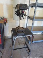 Full view of Black & Decker drill press mounted on rolling metal table with ball feet, showing drill press column, lever, metal work table, and base structure.