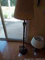 Full view of the floor lamp showing dark metal base with marble, standing on hardwood floor near patio door.