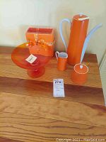 Orange Lefton tea pot, sugar bowl, creamer, napkin holder, and pedestal bowl arranged on wooden surface