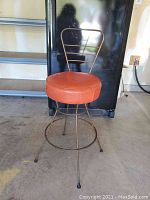 Full view of the metal framed swivel stool with orange vinyl round seat, showing the metal frame base, four legs with rubber feet, and backrest design.