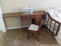 Wooden sewing machine cabinet set against wall, featuring attached Pfaff 260 sewing machine and wooden chair in front