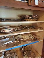 Multiple silverplate and aluminum serving trays, some with hammered texture and tarnished surface, displayed on shelves.