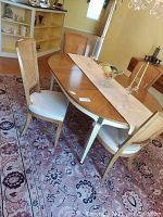 Full view of the vintage dining table with two leaves, surrounded by four caned back chairs with cushions, set on a patterned area rug in a room.