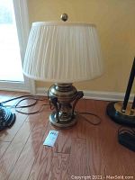 Full view of the brass urn table lamp with white pleated fabric shade showing its height and details of the base and shade.