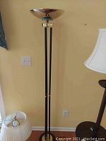 Photo of the full torchiere floor lamp showing tall slender black and brushed metal design standing against a beige wall.
