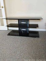 Full view of the three tiered TV stand showing black metal frame and tinted tempered glass shelves with cable cutouts.