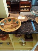 Wooden salad bowl, salad servers inside the bowl, and wooden cutting board with handle placed on counter.