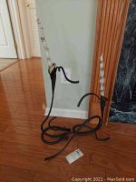 Set of two wrought iron candle holders with tall candles, standing on wooden floor against wall.