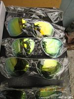 Several adult-sized sunglasses individually wrapped in plastic with reflective yellow-green mirrored lenses, shown stacked and packed in a box