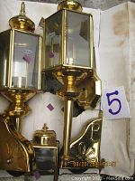 Photo showing two large solid brass and glass wall lanterns with intricate bases and clear glass panes.