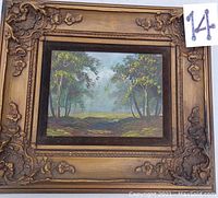 Full view of the signed landscape painting on canvas with ornate outer frame and dark inner frame, showing tree scenery and misty background.