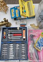 Top-down view showing drill driver, yellow drill bits case, socket wrench set, X-Acto blades, and various hand tools and accessories.