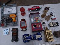 Photo showing soldering gun and various toy cars including a blue racecar and red sports car, decorative lanterns, mini arcade crane game, and small pottery and figurines.