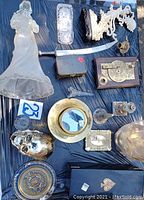 Overall view of all items spread on a dark surface including glass angel statue, brass mirror, skull, carved angel, and other collectibles.