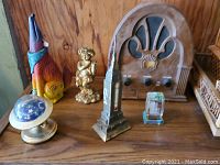 Photo showing a ceramic howling coyote, brass cherub figurine, antique wooden radio, Empire State Building thermometer, and a crystal block on a wood surface.