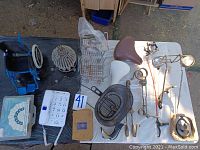 Overhead view showing leather and white bike seats, wire baskets, brown and black bike parts, doll-sized wheelchair, shopping carts, toy and lighting items, and large white house phone.