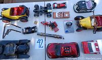 Wide view of various replica toy cars on a white table including vintage motorcycles, racing cars, and an electronic red car with control panel on roof. Also includes small bikes, emergency vehicle, and a wireless device in packaging.