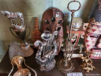 Photo showing lot contents including brass cobra incense burner, two carved wooden masks, horse trophy, crystal and brass pitcher, lyre-shaped candle holder, hanging candle holder, silver container, wooden puzzle, gold-tone branch sculpture.