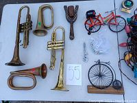 Photo showing three brass horns, wooden slingshot, two miniature collectible bicycles, black metal bicycle decor piece, miniature glass and ceramic toys, and framed vintage car print