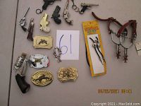 Photo showing various cowboy-themed belt buckles, toy gun belt buckles, and stirrup replicas with leather straps arranged on a flat surface.
