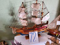 Photo showing a large wooden clipper ship model with white fabric sails, detailed rigging, and two masts. The model is mounted on a wooden base with a number 72 card in front.