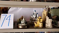 Shelf with various miniature castles made of resin or plaster in different colors and shapes including a white castle with blue rooftops