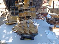 Overview of several wooden model ships with sails and rigging in various states, displayed on white table