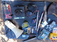 Full overhead view of all items in the lot spread on a black surface, showing megaphone, radios, cords, telescope fishing pole, leather helmet and small items.