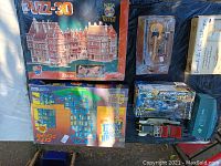 Top view showing various boxed kits including large 3D puzzle, blue construction kit, toy car, miniature guitar, and Leonardo DaVinci helicopter kit.