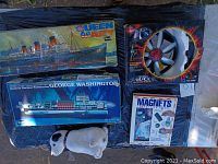Photo of Queen Mary and George Washington submarine model kits, Magnet Detective Files, Remote-Control Saucer toy, and a small plush dog toy on a black surface.