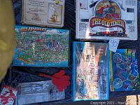 Top view of lot items including boxed Old Timer train set, Los Angeles cityscape puzzle, DaVinci helicopter kit box, and other packaged puzzles and accessories