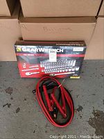 Front view of GearWrench socket set box and red and black jumper cables coiled in front