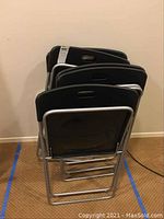 Five black folding chairs stacked together, metal frames visible, showing back and seat design.