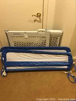 Photo showing folded Fisher Price baby safety gate and blue and white child bed rail leaning against wall.