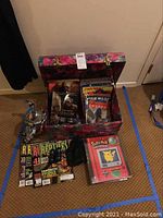 Photo of a floral-print storage box filled with Star Wars-related magazines and other items including a Pokémon card pack and wildlife magazines on the floor next to it.