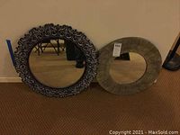 Both round mirrors placed on floor against wall, showing different frame styles and sizes.