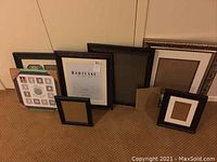 Seven picture frames of different sizes and styles arranged on floor against wall.