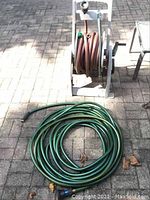 Overview of green garden hose coiled on ground with nozzle and brown hose reel with hose coiled on it.