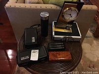 View of all items on brown round wooden table including humidors, cigar case, container, and clock in background.
