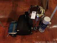 Room view of coffee urn, thermos, and two bags on hardwood floor under table