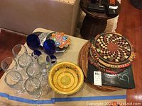 Overall view of placemats, trivets stacked, blue glasses, clear glass mugs and decorative plates on table