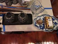 Photo showing two black and white patterned candles on a black rectangular tray, a clear glass vase with wavy rim, a blue and white decorative plate holding a turtle figurine and a small box.