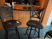 Two metal frame bar chairs with black leatherette seats and X-back design shown together near a counter.
