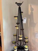Full view of the metal candle holder showing the structure with multiple candle cups and the bird figurine on top.