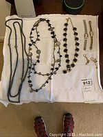 Full lot image of all jewelry items laid out on white cloth, including necklaces, watches, and earrings.
