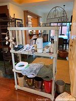Plastic rack unit with household items on shelves including fabric pieces, metal containers, a humidifier or similar device, and cables.